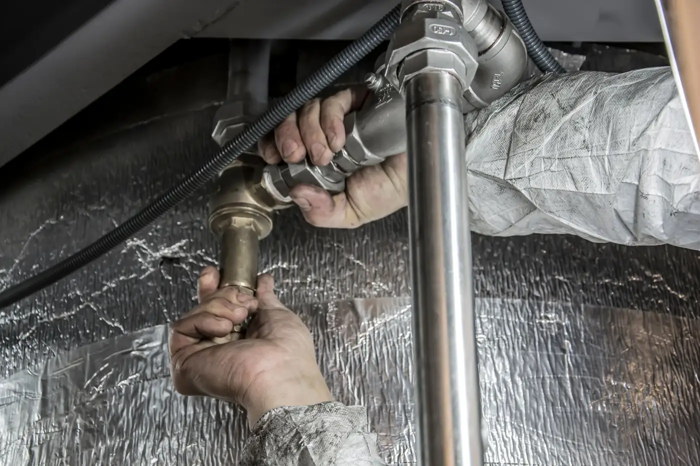 Illustrative photo of hands joining brass and silver pipe fittings. Not McNab Plumbing staff or a McNab job.